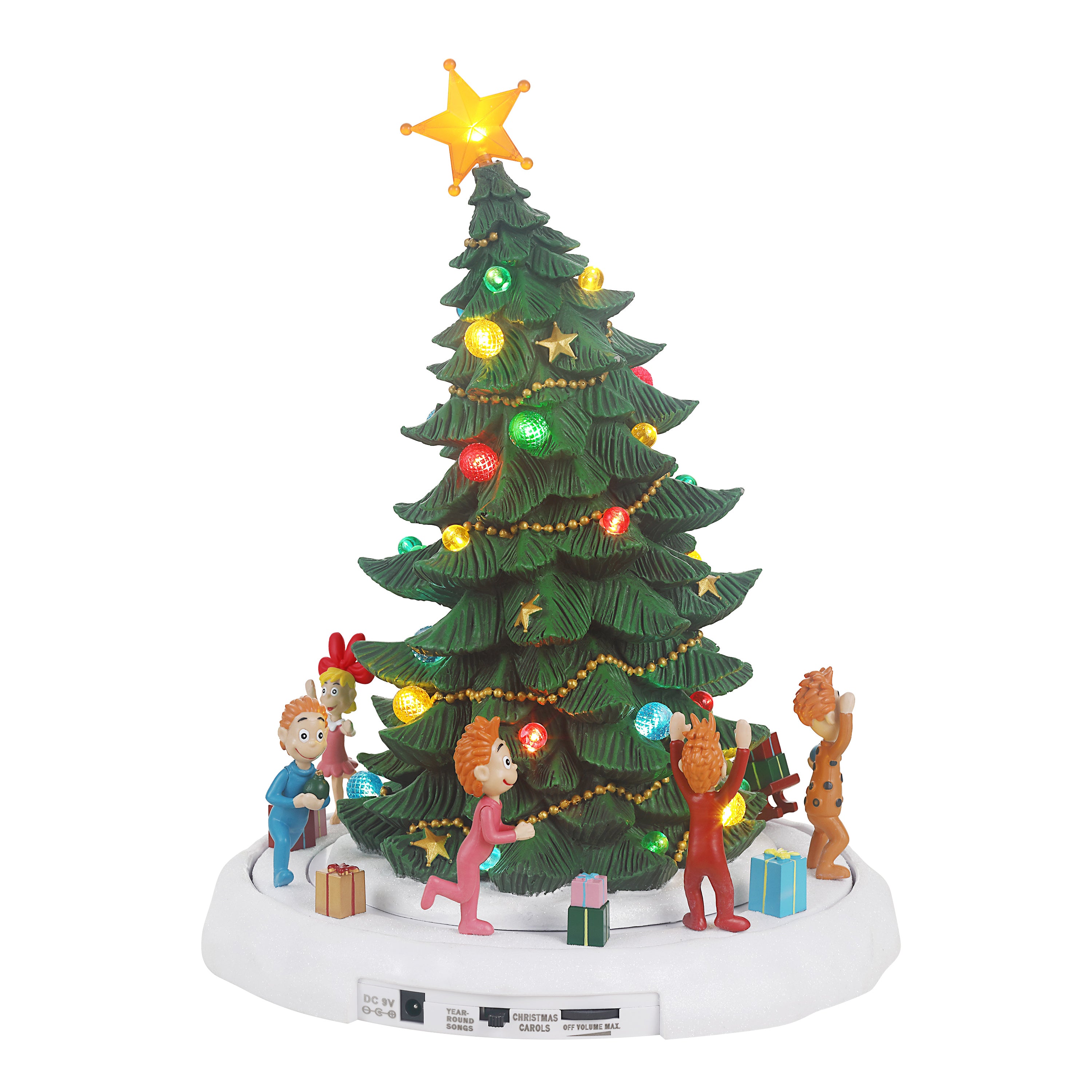 A lit Christmas tree tabletop decoration with a green tree, multicolored ornaments and lights, a glowing gold star on top, and small holiday figures and gifts around the base, shown on a white background.