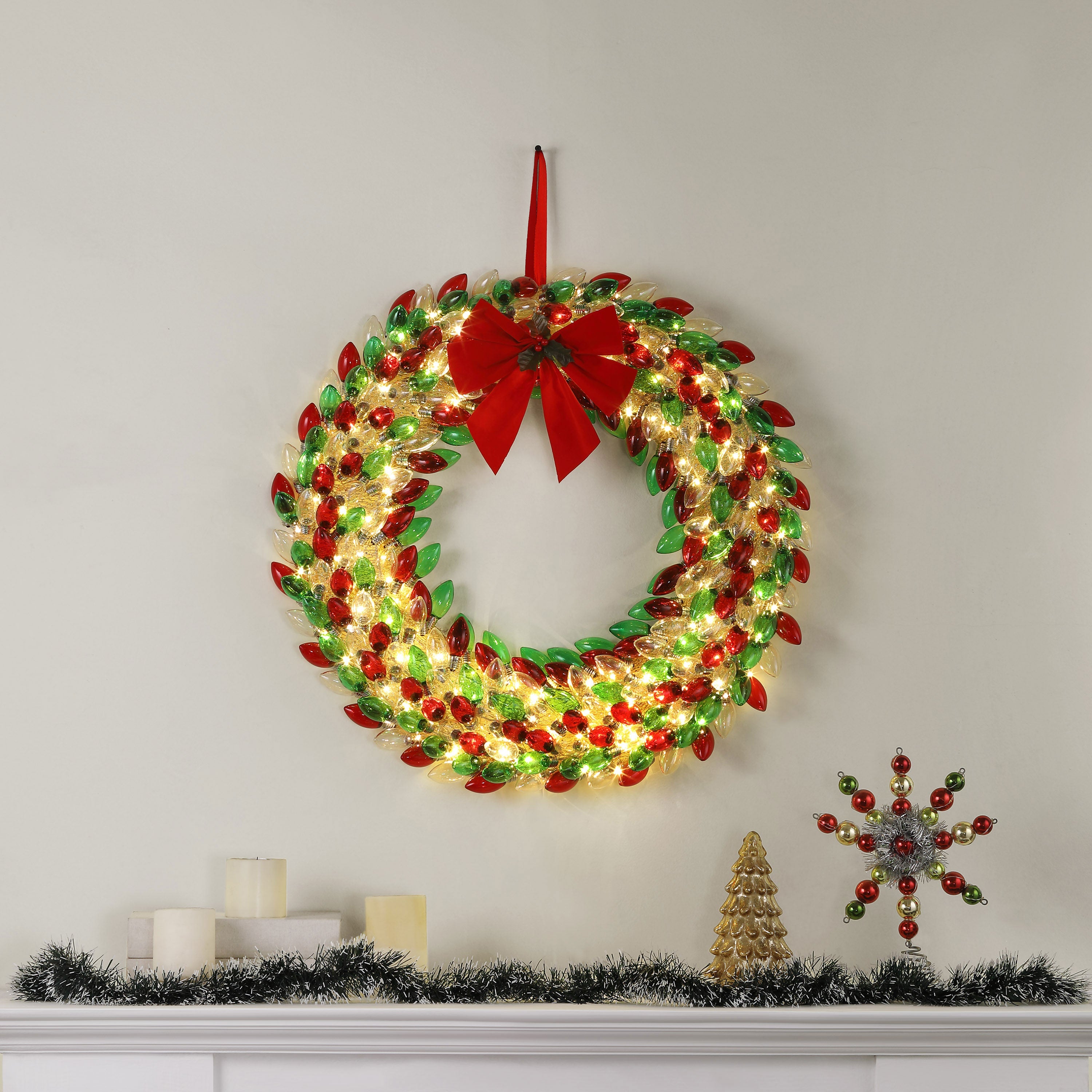 Mr. Christmas 30 in. Retro C9 Bulb Wreath with red and green colors hung on wall with festive decor on a mantel place