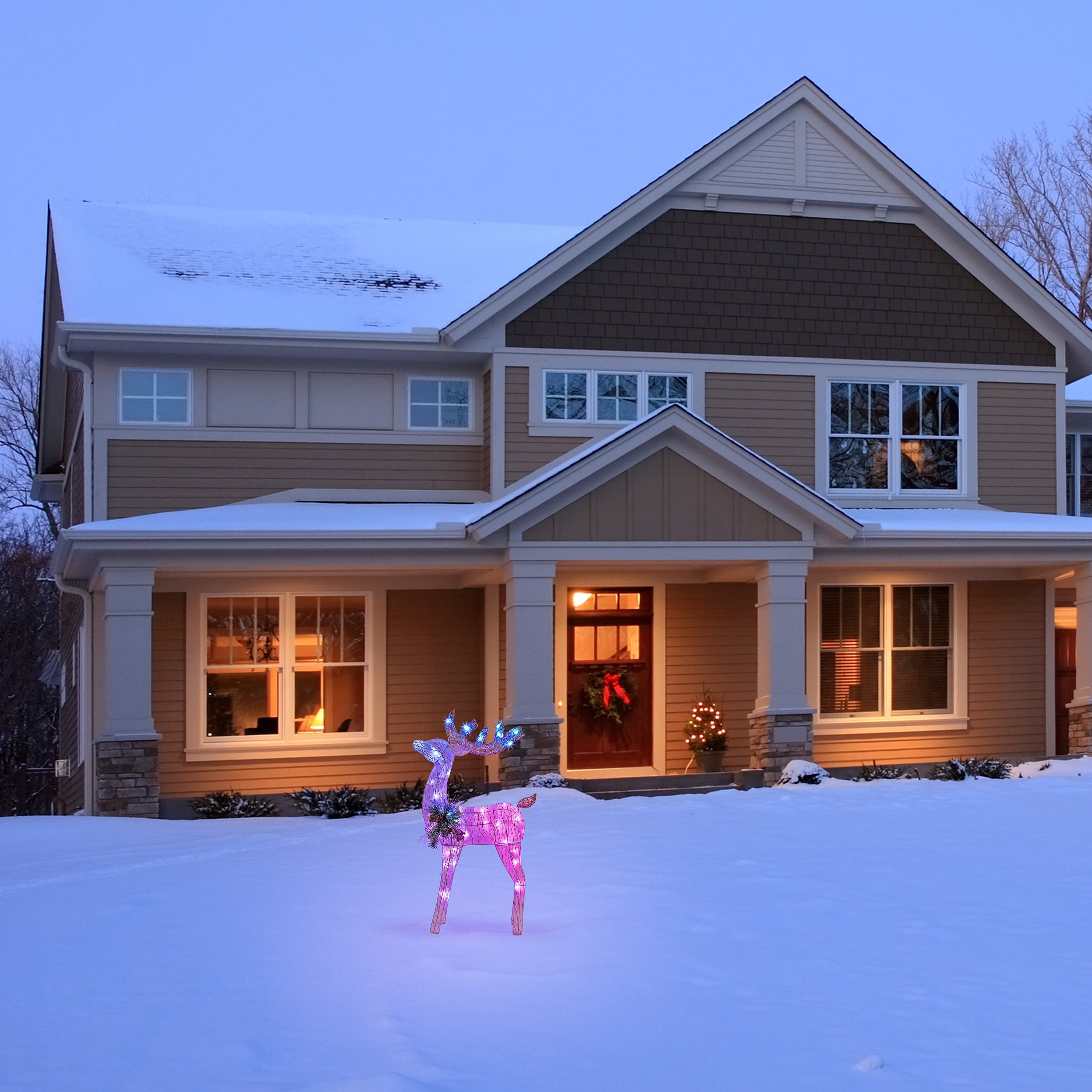 Full view of Mr. Christmas Fiber-Optic Reindeer in snowy yard, glowing beside a festive home during the holidays.