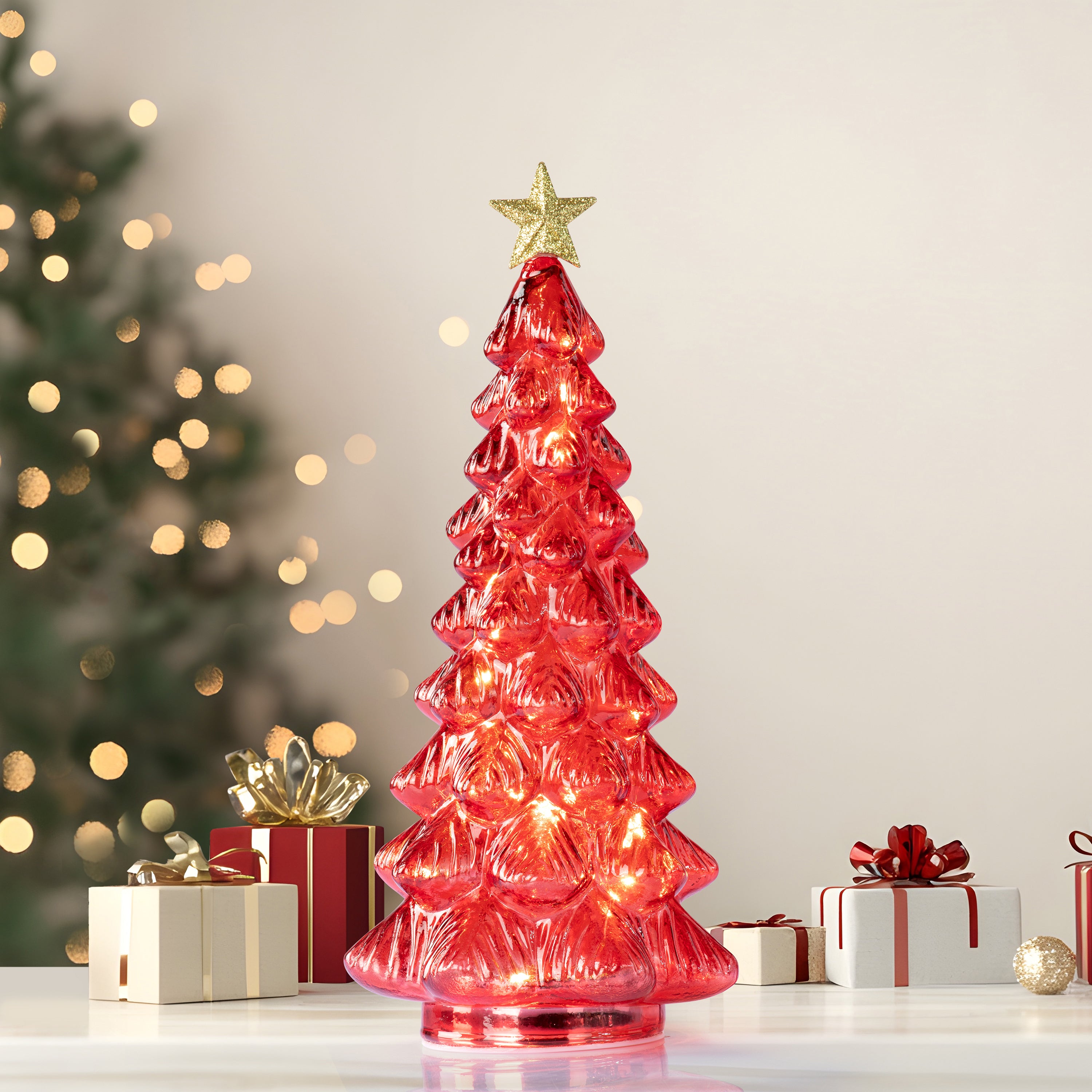 A red translucent glass Christmas tree light with a gold star topper in a festive background with presents
