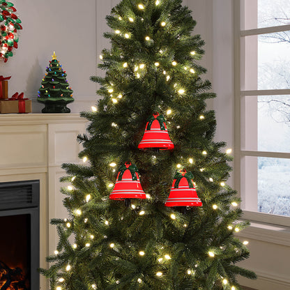 A Christmas tree in a living room setting, decorated with warm white string lights and three red bell ornaments with green hems.