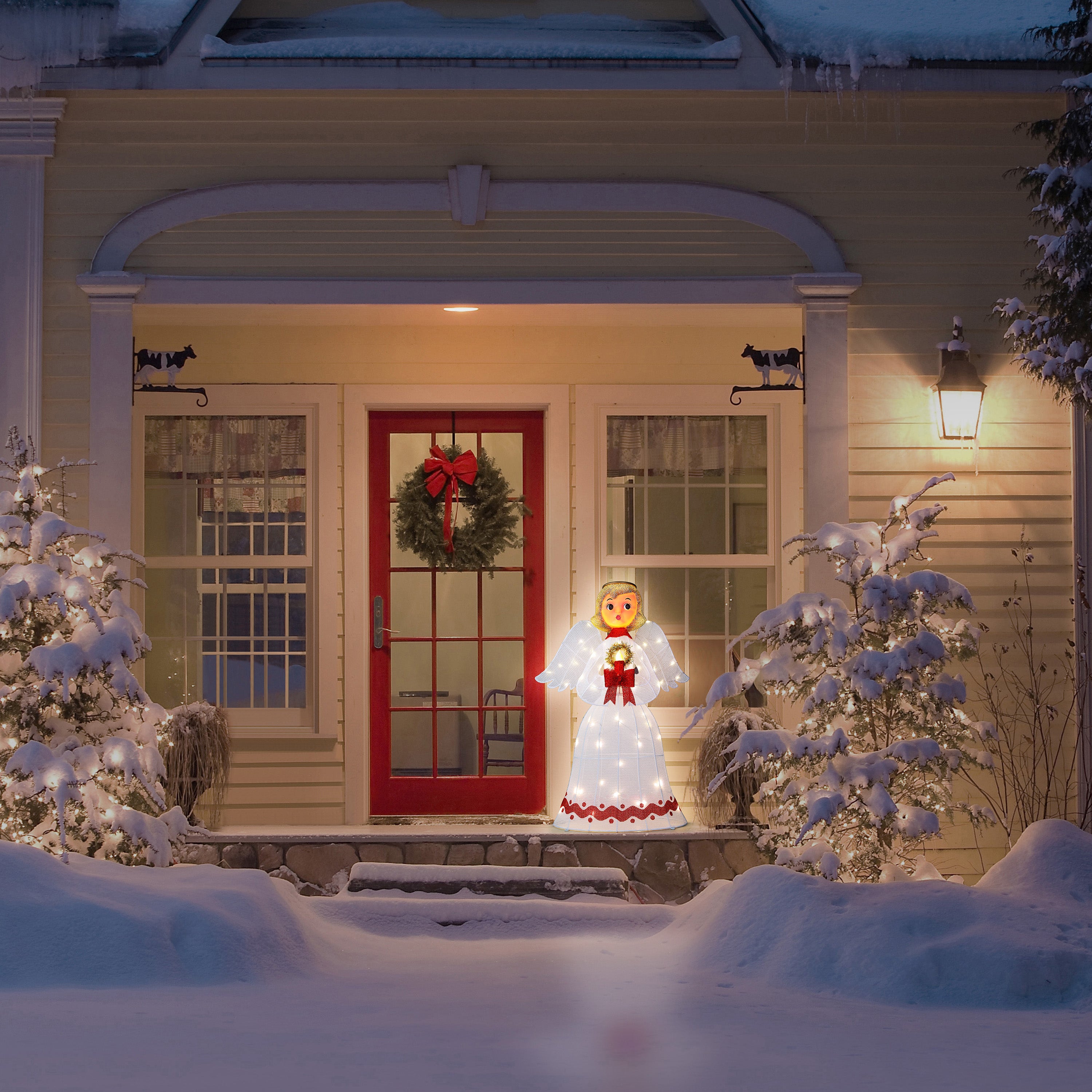 Decorative angel light on a snowy porch with a red door and wreath.