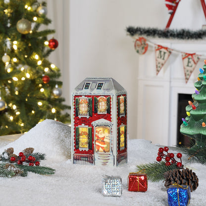 Decorative Christmas house light in a snowy scene with a Christmas tree and fireplace in the background.