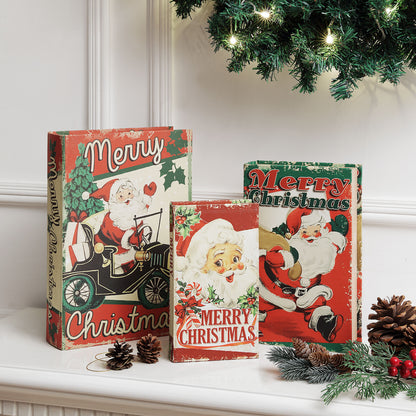 Three vintage-style Christmas book covers or decorative book boxes displayed on a mantel, featuring Santa Claus illustrations and Merry Christmas text, with pinecones, evergreen branches, and a Christmas tree branch in a holiday setting.