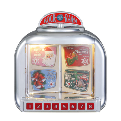 A Rock-Rama 8-slot Christmas music jukebox with a chrome silver body and red top sign. The front features four colorful holiday-themed card designs (Santa, angels, bells, and Christmas scenes) and a row of red numbered buttons 1 through 8.