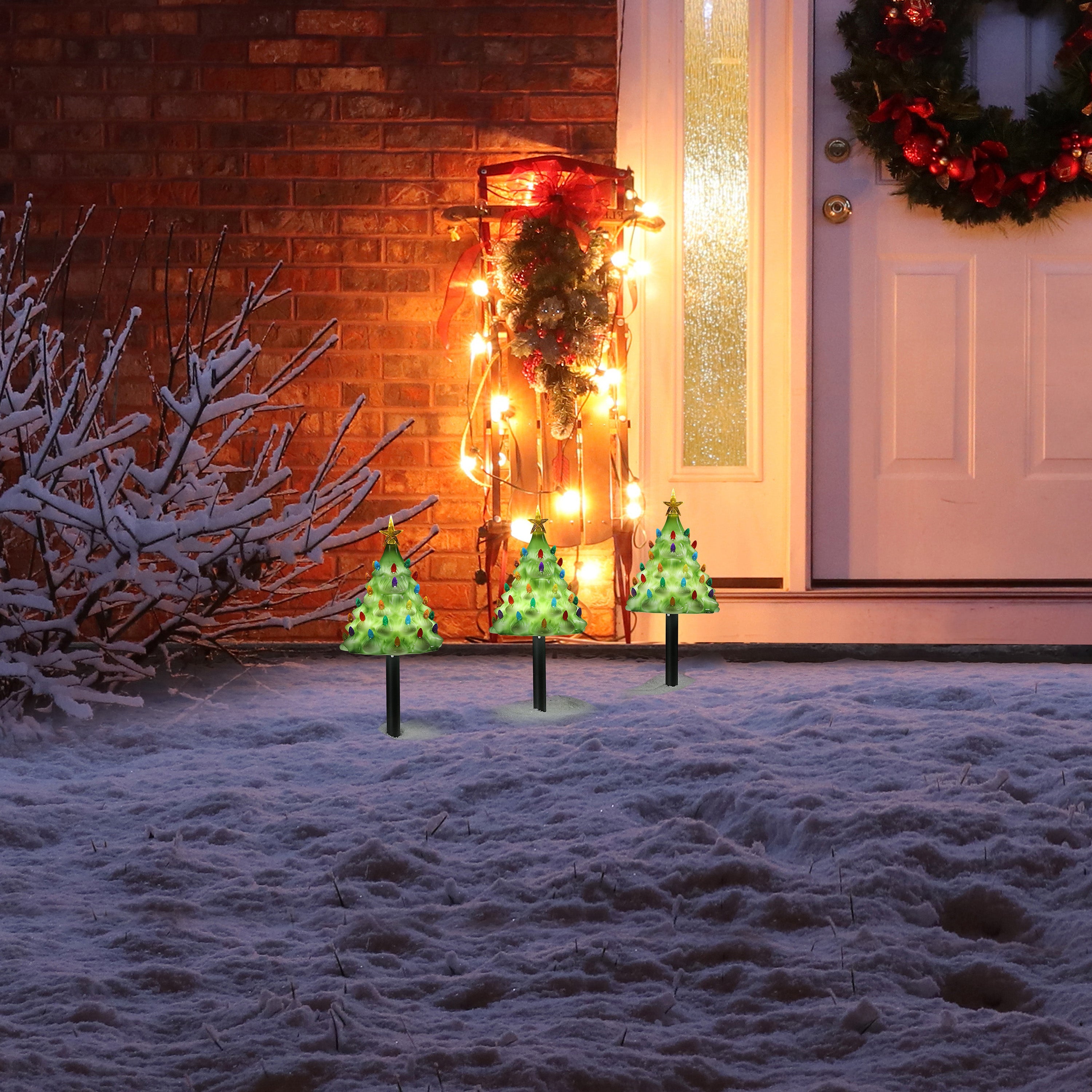 Mr. Christmas Lit Blow Mold Pathway Trees set up outdoors on snowy ground, glowing with multicolor bulbs and illuminated stars.
