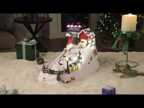 Load video: Video of Mr. Christmas Winter Wonderland Alpine Slalom in a festive background with animated skiers racing down the slope, LED lights glowing, and Christmas music playing in a snowy village scene