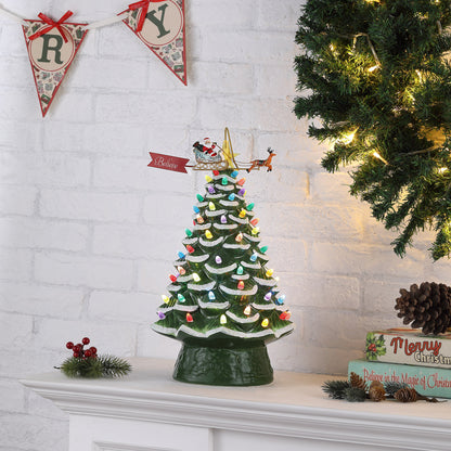 Green ceramic Christmas tree with Santa sleigh topper lit with multicolor bulbs on holiday mantel